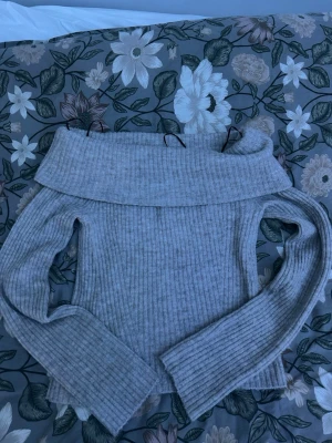 Ljusgrå off shoulder stickad tröja - Trendig ljusgrå stickad tröja från H&M med bred off shoulder-krage och ribbad struktur. Perfekt för dig som gillar en avslappnad men ändå snygg stil. Långa ärmar och mjukt material som känns skönt mot huden.