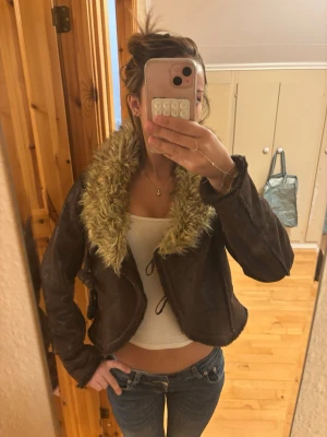 Brun pälsjacka med stor krage - Snygg brun pälsjacka med stor fluffig fuskpäls-krage i beige. Jackan har croppad passform och knytning framtill. köpte den för 600kr och säljer för att jag aldrig använder den