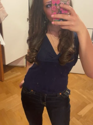 Mörkblå omlottopp med v-ringning från Nelly - Snygg mörkblå omlottopp med v-ringning och korta ärmar. Toppen har en figurnära passform och är perfekt att styla med jeans eller kjol. Enkel men elegant design som passar till många olika looks.