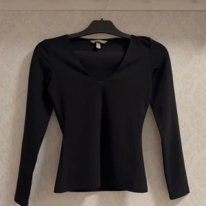 Svart långärmad v-ringad topp - Snygg svart topp med v-ringning och långa ärmar. Modellen är figurnära och passar perfekt till jeans eller kjol. Perfekt basplagg för alla tillfällen.