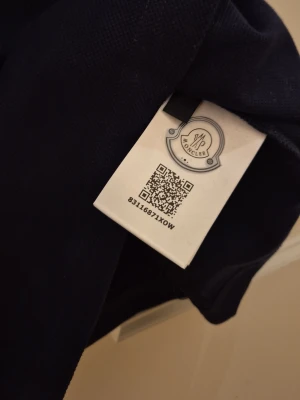 Mörkblå pikétröja från Moncler - Klassisk mörkblå pikétröja från Moncler med korta ärmar och krage. Tröjan har knappslå framtill och en diskret Moncler-logga på bröstet. Perfekt för en stilren och avslappnad look.