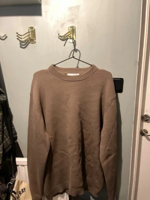Beige stickad tröja med rund hals - En enkel och stilren beige stickad tröja med rund halsringning och långa ärmar. Tröjan har en rak passform och ribbstickade muddar vid ärmslut och nederkant. Perfekt för lager-på-lager under kyliga dagar. Enbart testad. Säljer pga för stor.