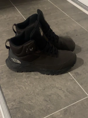 Svarta kängor från The North Face - Svarta kängor från The North Face med snörning och robust sula. Tillverkade i slitstarkt material med hög ankel och logga på sidan och plösen. Perfekta för kyligare väder och outdoor-aktiviteter.