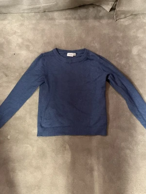 Blå stickad tröja från VILA - Snygg blå stickad tröja från VILA med rund halsringning och ribbade muddar vid ärmslut och nederkant. Tillverkad i mjukt material för en bekväm känsla.