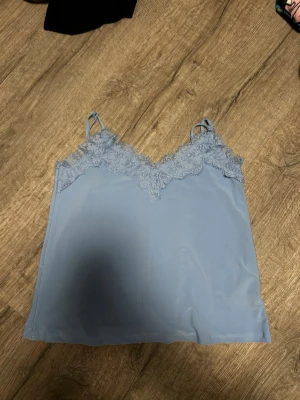 Ljusblå spetslinne med tunna band från new yoker  - Snyggt ljusblått linne med tunna axelband och spetsdetaljer längs v-ringningen. Väldigt tunt och skönt matreial.