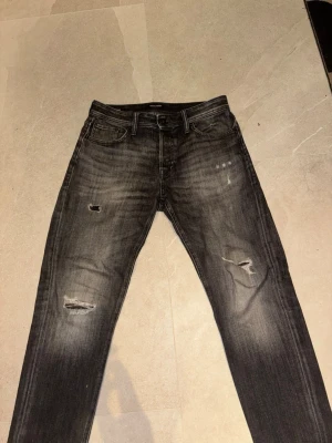 Svarta slitna jeans med raka ben - Snygga svarta jeans med slitningar och lätt tvättad look. Jeansen har raka ben och klassisk femficksdesign. Perfekta för dig som gillar en lite tuffare stil. Materialet är jeans och färgen är mörkgrå till svart.