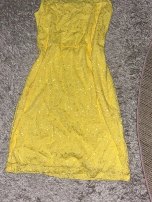 Gul spetsklänning från Miss Classic - Snygg gul kortklänning från Miss Classic med vacker spets och figurnära passform. Klänningen är ärmlös och har ett elegant spetsmönster som ger en romantisk känsla. Perfekt för sommarens alla tillfällen!