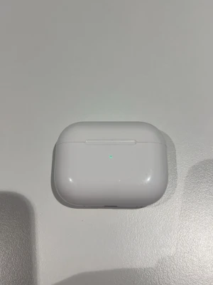 Apple AirPods Pro trådlösa hörlurar - Säljer ett par vita Apple AirPods Pro med laddningsetui. De är kompakta, har en stilren design och sitter bekvämt i öronen. Perfekta för musik, poddar och samtal. Laddningsetuiet är i blank plast och har en liten LED-indikator på framsidan.