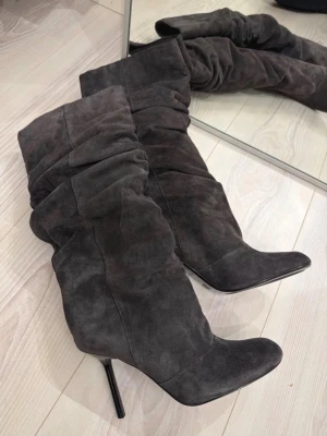 Gråa stövletter i mocka från Zara - Snygga gråa stövletter från Zara i mjuk mocka med hög smal klack och spetsig tå. Skorna har en slouchy design som ger en trendig look och passar perfekt till många outfits.