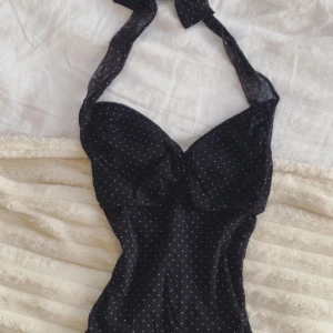 2000 talet svart prickig halterneck topp med knyt - Skit snygg svart halterneck topp med vita prickar och knyt i nacken, som kan knytas till en söt rosett. Den har lätt vadderade kupor och en liten scrunch framtill. Har tyvärr ingen lapp men den var min mammas från 2000s talet! Skulle säga att den är storlek xxs-xs. Materialet är lite mesh. Den sitter så fint på kroppen och gör en snatched ⏳💕