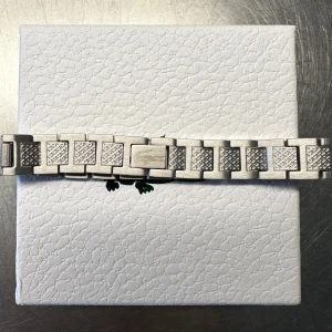 Silverfärgad armband från Lacoste - Stilren armband i silverfärgat metall från Lacoste. Länken har ett coolt mönster på länkarna och robust design som ger en modern känsla. Perfekt för dig som vill uppgradera din klocka med en snygg och tidlös look.