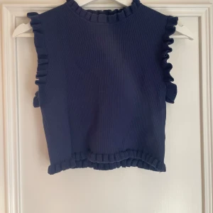 Kort marinblå topp med volanger - Kortare modell i marinblått med volanger. Använd varsamt ett fåtal gånger