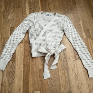 Beige omlottkofta från NA-KD - Superfin beige omlottkofta från NA-KD med knytband i midjan och stickad struktur. Koftan har lång ärm, v-ringning och är i ett luftigt, stickat material som känns både trendigt och bekvämt. 