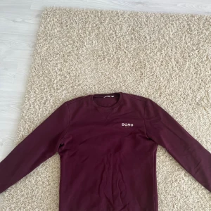 Vinröd tröja från Björn Borg - Säljer en vinröd långärmad tröja från Björn Borg med rund halsringning och diskret logga på bröstet. Tröjan är i mjuk bomull och har en klassisk, enkel design som passar perfekt till jeans eller joggers. 