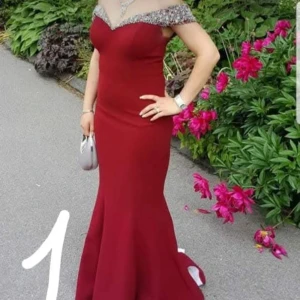 Vinröd långklänning med silverdetaljer - Säljer en elegant vinröd långklänning med offshoulder och silverglittrande detaljer vid halsringningen. Klänningen har en figurnära passform och en vacker utsvängd nederdel som ger en lyxig känsla. Perfekt för bal eller fest.