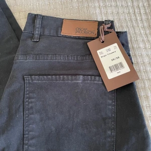 Oscar Jacobson Jeans - Svarta jeans från Oscar Jacobson med klassisk femficksdesign och snygga kopparfärgade nitar. Byxorna har rak passform och är tillverkade i mjuk bomull med en stilren look. Perfekt för dig som gillar tidlös och enkel stil.
