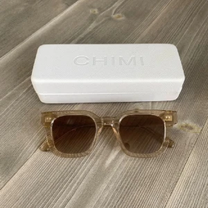 Beige CHIMI solglasögon Ecru - Snygga fyrkantiga solglasögon från CHIMI i modellen Ecru 04. Bågarna är transparenta i beige ton och har bruna tonade glas. Ramen är i plast och designad i Stockholm. Perfekt accessoar för en clean och modern look.