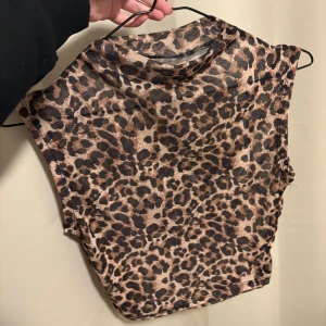 Leopardmönstrad mesh topp - Säljer en ärmlös mesh topp med leopardmönster i bruna och svarta toner. Toppen har en hög hals och är lätt transparent, perfekt för att skapa en edgy look. Passar dig som vill sticka ut med djurprint och cool stil.