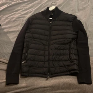  Moncler jacka - Svart pufferjacka från Moncler med quiltad front och släta ärmar. Jackan har två sidofickor med dragkedja, ribbad krage och Moncler-logga på ärmen. Materialet är dunfyllt med certifierad kvalitet enligt DIST. Perfekt för dig som vill ha en clean och stilren look. Säljer den nu billigt för jag vill bli av med den o köpa något nytt!