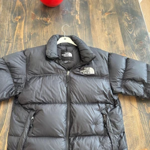 Svart pufferjacka från The North Face - Säljer en svart pufferjacka från The North Face med klassisk logga på bröstet och ryggen. Jackan har hög krage, två sidofickor med dragkedja och quiltad design. Perfekt för kalla dagar och har en riktigt schysst oversized vibe.
