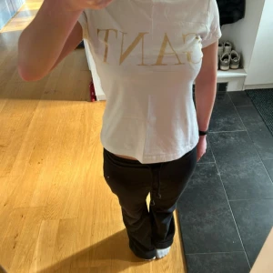 Vit GANT t-shirt med guldtryck - Snygg vit t-shirt från GANT med stort guldigt logotryck på bröstet. Modellen är klassisk med rund hals och korta ärmar. Materialet är mjuk bomull som känns skönt mot huden. Passformen är normal.