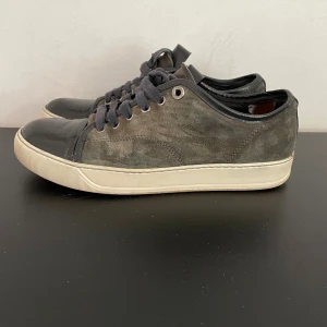 Lanvin skor - Snygga sneakers från Lanvin i mörkgrå mocka med svarta skinn-detaljer på tån och svarta snören. Fint skick 7-8/10. Pris kan diskuteras. Hör av er vid frågor! Storlek 39,5 men passar 40,5. Rekommenderad storlek är 1 större. Dustbag samt box ingår! Enda defekten är bak i hälen