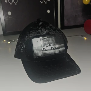 Velvet keps - Svart truckerkeps med mesh på baksidan och ett stort svartvitt tryck av en sportbil framtill. Kepsen har böjd skärm och justerbar passform. Materialet är syntet och polyester, vilket ger en lätt och luftig känsla. Perfekt för dig som gillar streetstyle och bilar. Köpt på hatstore för 399kr