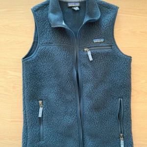 Blå fleeceväst från Patagonia - Säljer en blå fleeceväst från Patagonia med hög krage och tre praktiska fickor med dragkedja. Västen har en mjuk, fluffig yta och klassisk passform. Perfekt för lager-på-lager och outdoor-häng.
