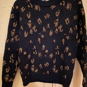 Svart leopardmönstrad stickad tröja - Svart stickad tröja med guldiga leopardmönster över hela plagget. Tröjan har rund halsringning och långa ärmar. Perfekt för dig som vill sticka ut med en cool och trendig look. Pris kan diskuteras