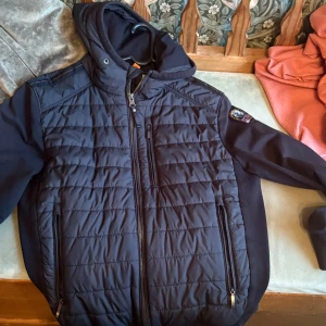 Svart quiltad jacka Parajumpers S - Svart quiltad pufferjacka från Parajumpers med huva och dragkedja. Jackan har flera fickor med dragkedja, patch på ärmen och sportig look. Tillverkad i syntetmaterial och polyester, perfekt för höst och vinter.inga håll eller fläckar eller nåt. Andväde lite förra hösten smart andvänd skriv om du har några frågor. Finns att hämta i Farsta eller så postar jag inga problem 