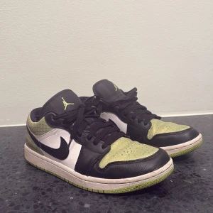 Nike Air Jordan 1 Low svart/grön 40 - Nike Air Jordan 1 Low sneakers i svart, vitt och ljusgrönt med coolt texturerat mönster på tå och häl. Klassisk Jumpman-logga i grönt på plösen, svart swoosh och snörning. Platt sula med gröna detaljer. Perfekt för dig som vill sticka ut med dina sneakers. Ovanlig lite svårare att få tag på.