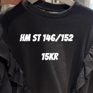Svart tröja med volang från H&M - Svart tröja från H&M i storlek 146/152. Tröjan har rund halsringning och snygga volangdetaljer längs ärmarna som ger en cool och trendig look. Perfekt för dig som gillar stilrena plagg med en twist.
