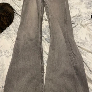 Grå bootcut jeans från Gina Tricot - Snygga grå jeans från Gina Tricot i bootcut-modell. Jeansen har en klassisk femficksdesign och är tillverkade i mjukt denimtyg. Perfekt för dig som gillar en retro vibe och vill ha ett par jeans med lite extra vidd nedtill.