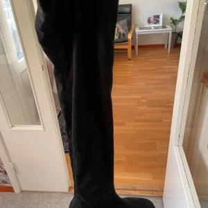 Svart overknee boots i sammet - En elegant svart Ove knee boots i mjuk sammet. Klänningen har en klassisk rak siluett och är perfekt för dig som vill ha en stilren och tidlös look. Passar dig som gillar minimalistisk stil och vill sticka ut med en lyxig känsla.