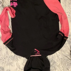 Svart och rosa hoodie från Argenta - Säljer en svart hoodie från Argenta med coola mörkrosa ärmar och tryck i rosa på bröstet. Tröjan har huva och är tillverkad i 100% bomull, vilket gör den skön och mjuk. Perfekt för dig som gillar streetstyle och vill sticka ut lite extra.