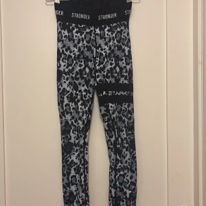 STRONGER Leopardmönstrade - Snygga svarta och grå leopardmönstrade leggings från Stronger med hög midja och elastisk logotypresår.  