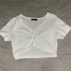 Vit croppad omlottopp från SHEIN - Säljer en vit croppad topp från SHEIN i storlek M. Toppen har omlottdesign med v-ringning och korta ärmar. Materialet är ribbad polyester som ger en skön och stretchig känsla. Perfekt för dig som gillar stilrena och trendiga plagg.