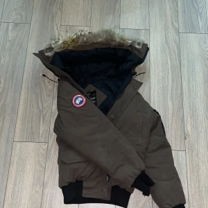 Brun Canada Goose dunjacka med päls - Säljer en brun Canada Goose dunjacka. Storleken är 3xs alltså passar för folk runt 170 men lite smallare runt magen och neråt, passar för ish 170, 55kg. Jackan är äkta men limet till pälsen har tårkat så det råkade ramla av lite bitar men inget som sker längre. Nypris 10 000  utan kvitto tyvärr men säljer den billigare än så. Hör av er vid olika frågor.☺️Va inte rädd o fråga om bättre priser 