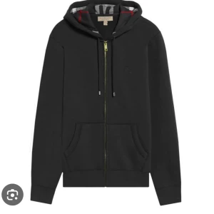 Svart hoodie från Burberry med huva - Svart hoodie från Burberry med dragkedja framtill, klassisk huva med snörning och fickor på magen. Insidan av huvan har Burberrys ikoniska rutiga mönster. Perfekt för dig som gillar stilrena och exklusiva plagg.