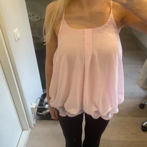 Ljusrosa volangig linnetopp - Säljer en ljusrosa linnetopp med tunna axelband och volangig nederkant. Toppen är luftig och har en ballongliknande form med dubbla lager tyg som ger en cool och lekfull look. Perfekt för dig som gillar romantiska och söta vibes.
