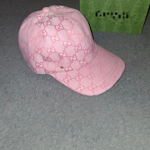 Rosa keps med GG-mönster - Snygg rosa keps med ikoniskt GG-mönster över hela kepsen. Justerbar rem i rosa läder baktill och liten guldfärgad GG-detalj framtill. Kepsen är tillverkad i bomull och har en klassisk böjd skärm. Perfekt för dig som vill sticka ut med lyxig streetstyle.