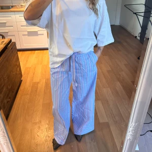 Blå- och vitrandiga wide byxor - Säljer ett par blåa byxor med vita och rosa ränder, loose fit och breda ben. Byxorna har snörning i midjan och är tillverkade i ett mjukt bomullsmaterial. Perfekta för en chill och avslappnad stil. Aldrig använda, lappen sitter kvar💓💓💓