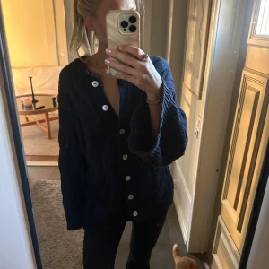 Mörkblå stickad kofta från Gina Tricot - Säljer en chunky mörkblå stickad kofta från Gina Tricot med grovt flätmönster och stora vita knappar. Koftan har lång ärm, ribbade muddar och en oversized fit som är riktigt cozy. Perfekt att slänga på sig när det är kyligt ute. Tröjan är använd ca 3 gånger och är i riktigt bra skick, pris kan diskuteras🥰