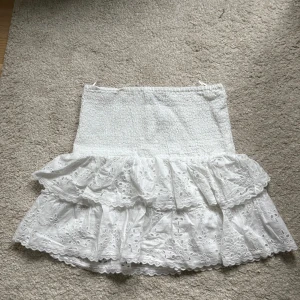 Vit volangkjol från Gina Tricot - Supersöt vit kortkjol från Gina Tricot med två lager volanger. Kjolen har broderade spetsdetaljer och är gjord i mjuk bomull. Perfekt för dig som gillar romantisk och feminin stil med extra volym.