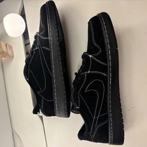 Nike Jordan 1 Low Travis Scott svart, FLER BILDER FINNS - Nike Jordan 1 Low Travis Scott i svart mocka med vita kontrastsömmar och broderad logga på hälen. Snygga detaljer som röd text på plösen och klassisk Nike Air-märke. Platt sula och rund tå, perfekt för dig som gillar streetwear och unika sneakers. SKRIV FÖR FLER BILDER
