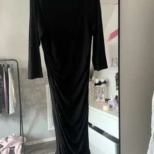 Svart långklänning med trekvartsärm - En svart långklänning med trekvartsärm och rund halsringning. Klänningen har en smickrande passform och är tillverkad i ett mjukt, stretchigt material som faller snyggt längs kroppen. Perfekt för dig som gillar en stilren och tidlös look.