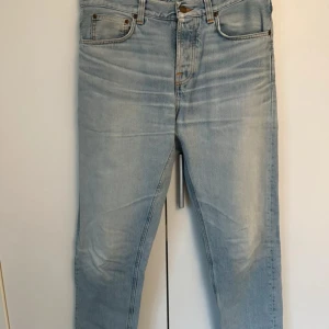 Ljusblå jeans från Nudie Jeans, steady eddie - ljusblå jeans från Nudie Jeans. Jeansen har broderad bakficka och normal passform. Tillverkade i bomull och perfekta för en avslappnad stil. Modell steady eddie och har en straight passform storlek 32/32 men uppklippt någon centimeter på benet. Liten fläck på ena låret som jag inte försökt få bort men märks knappast