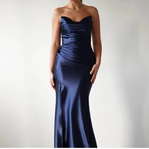 Marinblå axelbandslös långklänning - Säljer en marinblå axelbandslös långklänning i glansigt satinliknande material. Klänningen har figurnära passform, draperad överdel och en snygg slits framtill. Perfekt för bal eller festliga tillfällen. Sitter riktigt snyggt och ger en elegant siluett. Köpt för 1300
