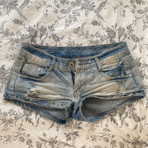Blå slitna jeansshorts med låg midja - Säljer ett par blå jeansshorts med låg midja och klassisk femficksdesign. Finns ingen lapp i men de är köpa på en marknad utomlands