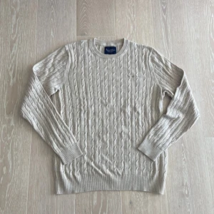Beige kabelstickad tröja från Bondelid - Snygg beige kabelstickad tröja från Bondelid med rund hals och ribbade muddar. Tröjan har ett klassiskt mönster och är tillverkad i mjuk bomull, perfekt för dig som gillar stilrena och bekväma plagg. Passar dig som vill ha en enkel men ändå trendig look.